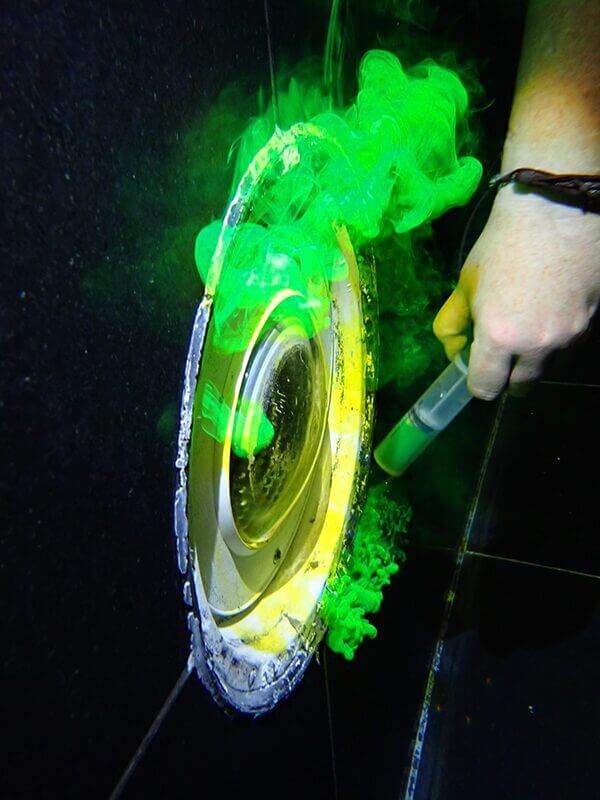 Image of someone dye testing a swimming pool with green dye to look for leaks